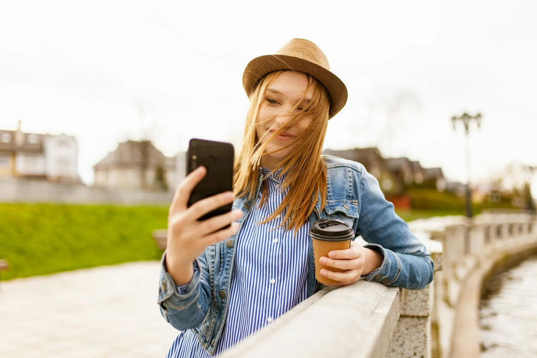 A person that is outside holding a cup while taking a picture of themselves with their phone.