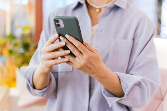 A person with a lilac button down shirt holding a phone.