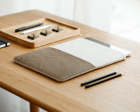 An iPad sleeve in a wood table with pencils, clips, and notebook.