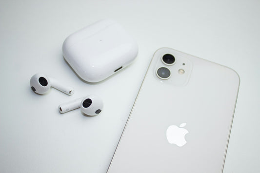 A White iPhone and AirPods laying on white table.